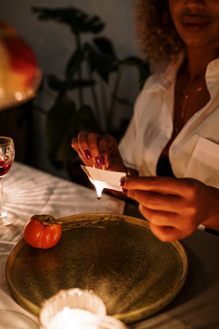 A serene candlelit dinner setting with a woman preparing the table, highlighting seasonal decorations and warm ambiance.