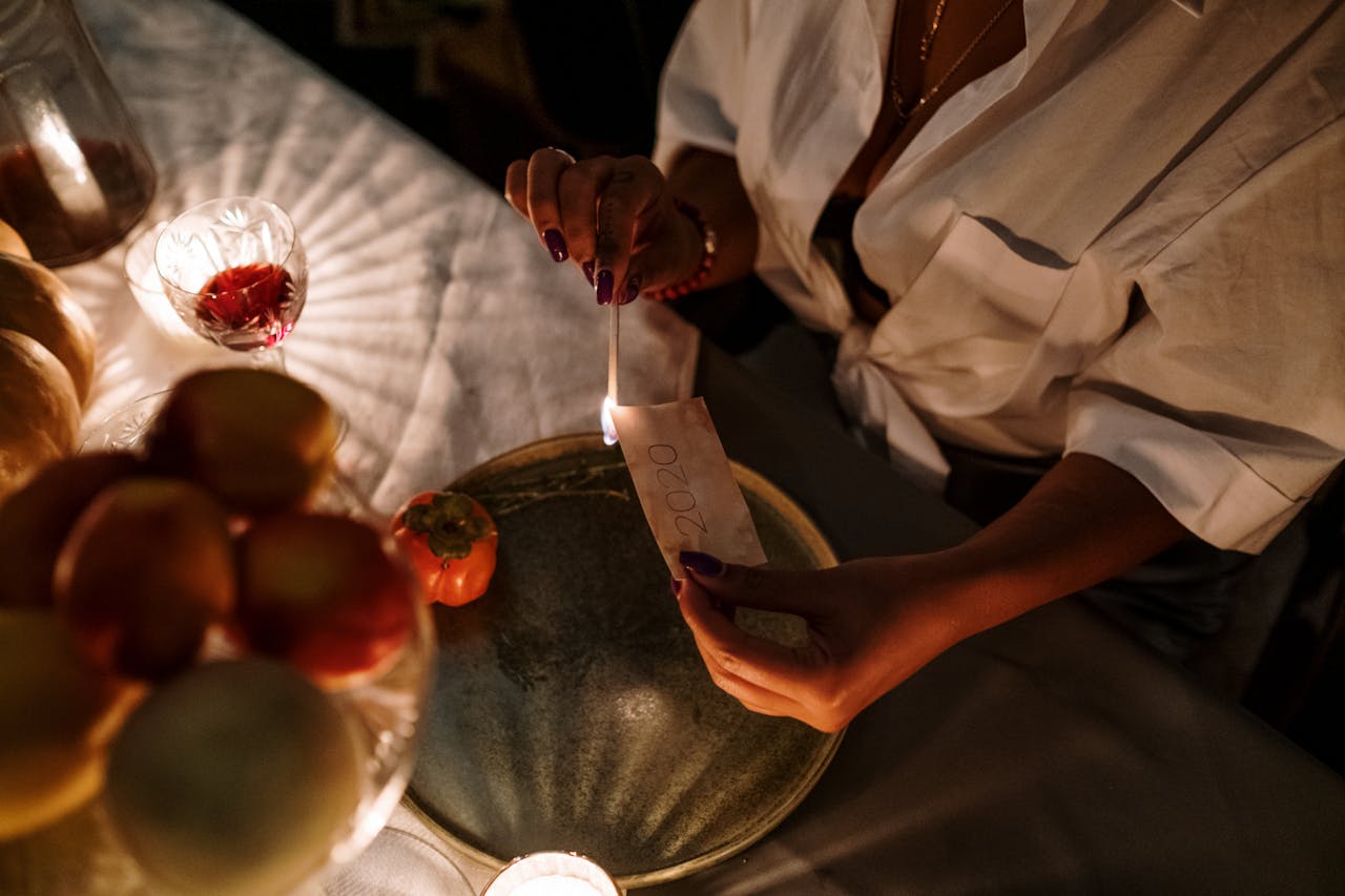 A woman sitting at a dining table, burning paper with a candle flame during a cozy evening ritual.